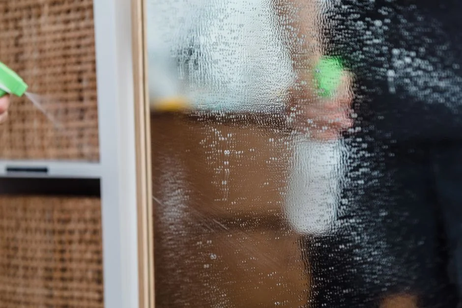 who-we-are A person wearing rubber gloves cleaning a dirty gas stove with a cloth and spray bottle.